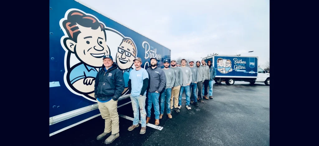 A line of gutter installation team members standing beside branded blue service trucks in a parking lot.