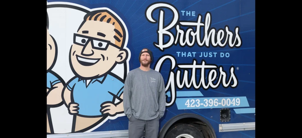 Team member standing casually in front of a blue gutter company trailer with large logo graphics.